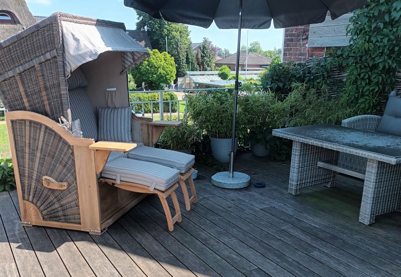 Ein Strandkorb steht auf einer Dachterrasse. Es sieht sehr sonnig aus.